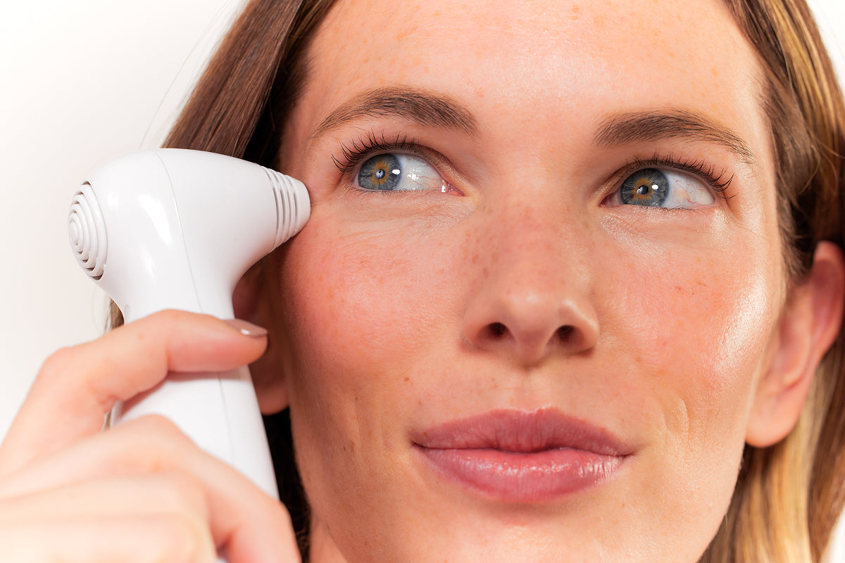 Close-up of a woman's face, showing her holding the white Nira Skin Laser device next to the delicate skin around her eye to reduce fine lines and crow's feet.