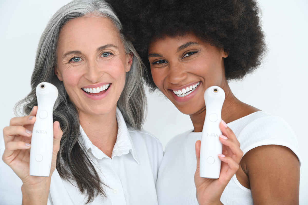Two smiling women, each holding a Nira Skin Laser, representing effective anti-aging treatment for all skin tones and mature skin.