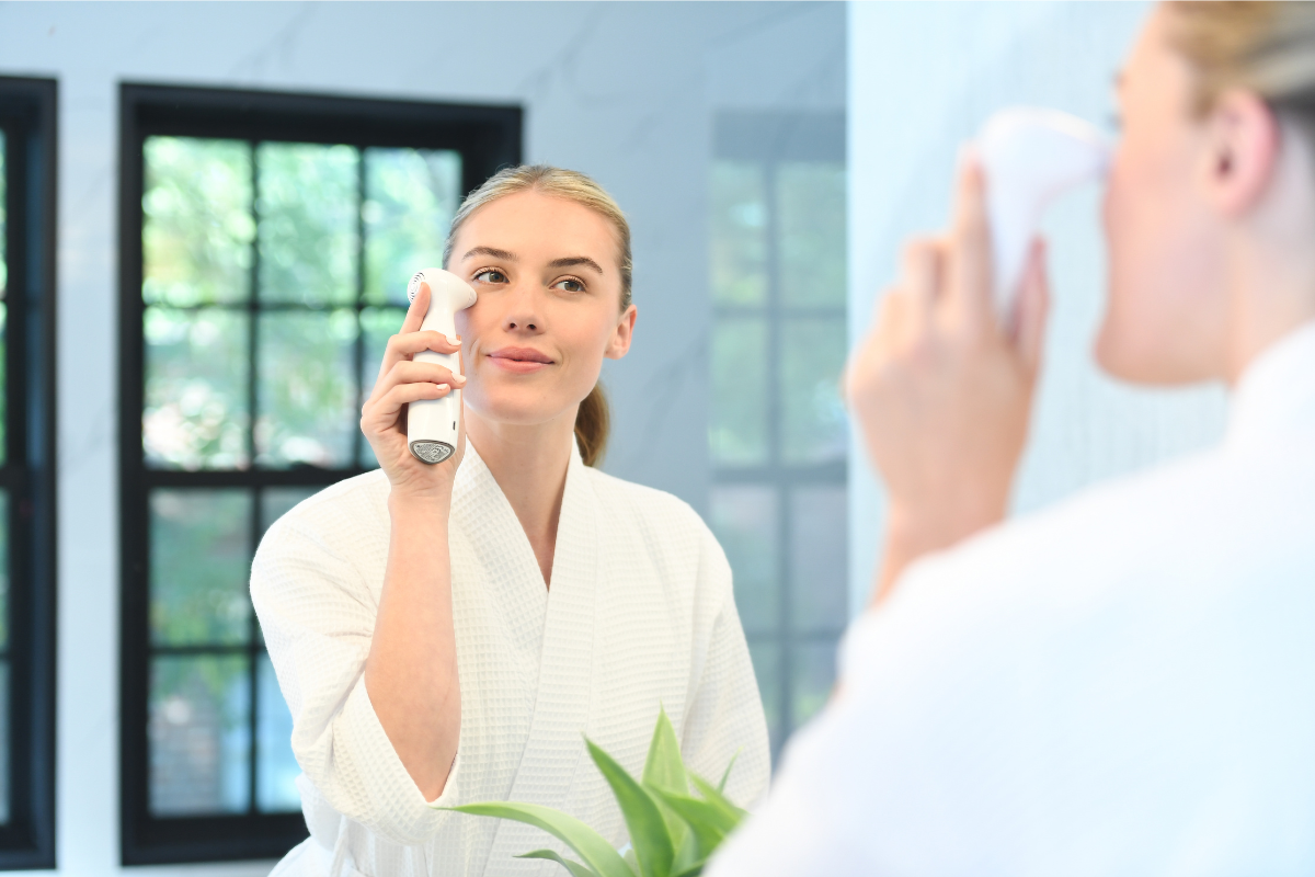Young woman using the NIRA at-home laser while looking at herself in the mirror, promoting skin rejuvenation and collagen renewal.