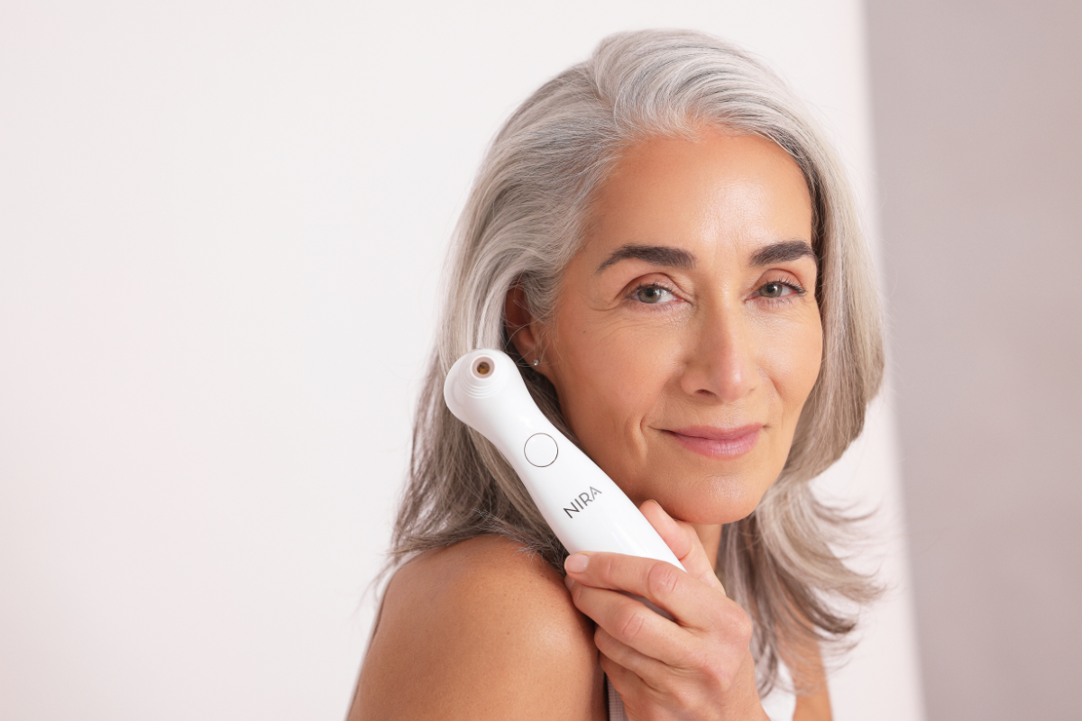 A woman with gray hair holding the NIRA Precision at-home laser device during her skincare routine.