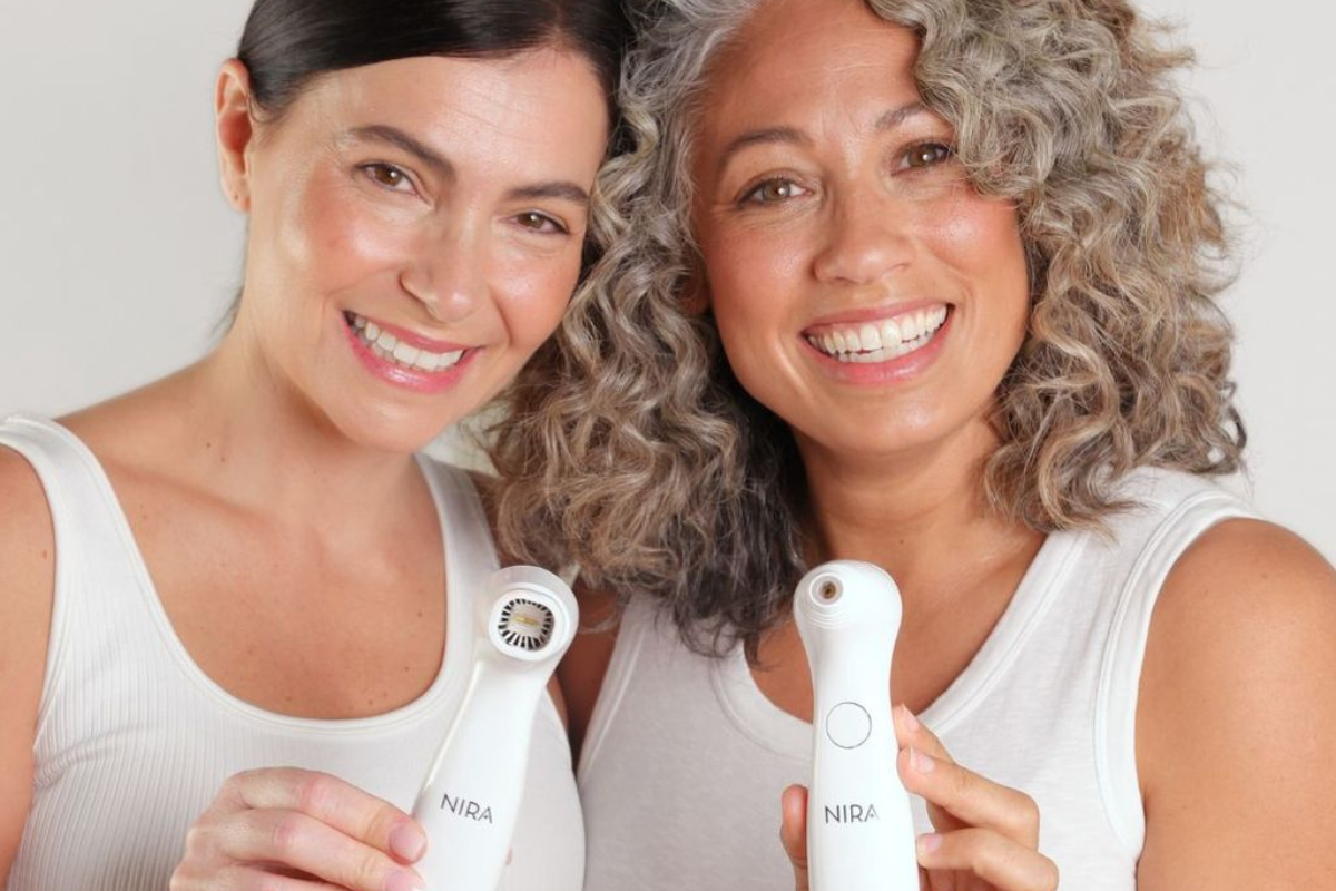 Two people of different ages holding a Nira at-home laser device, smiling and showing glowing, radiant skin together.