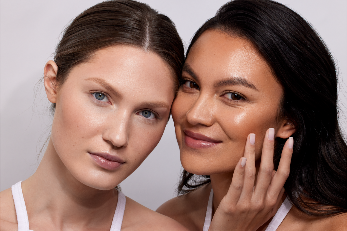 Two women standing side by side, smiling and embracing, showcasing radiant, youthful skin after using NIRA at-home laser skincare devices.