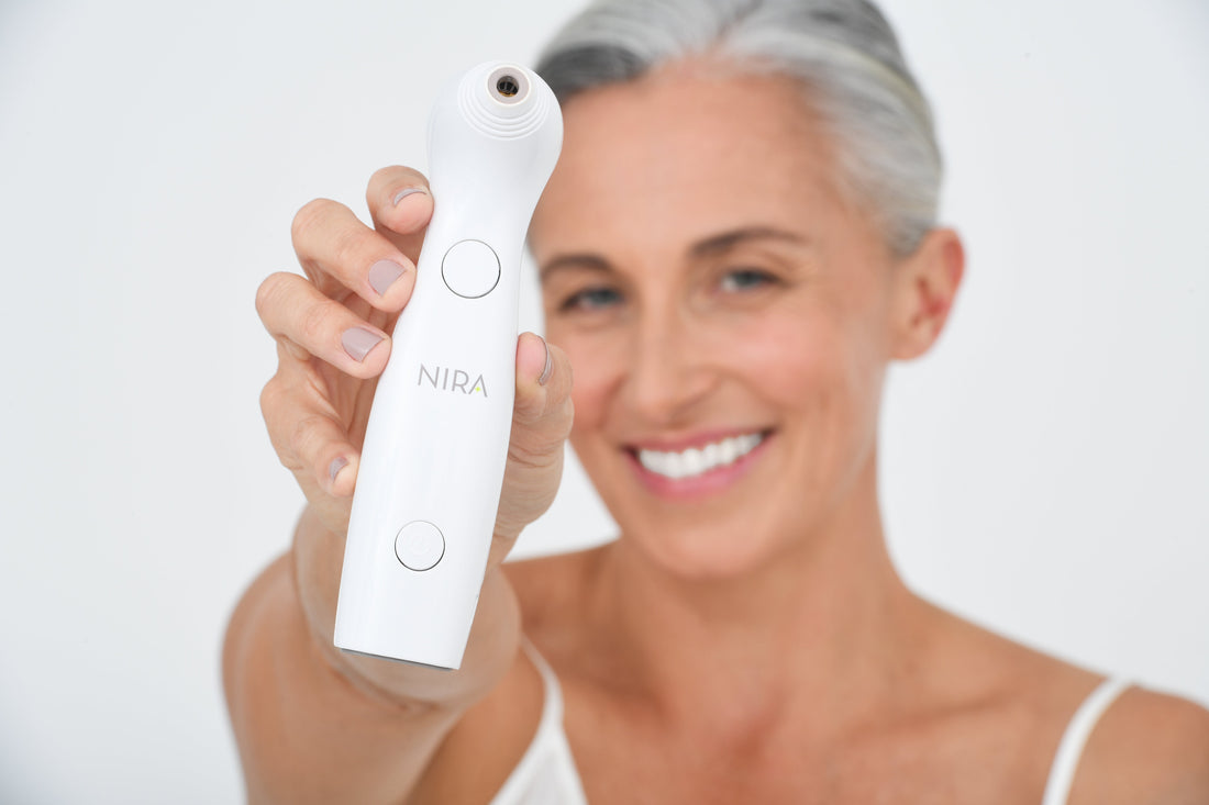 A woman with gray hair holding the NIRA Precision at-home laser device in front of her face during her skincare routine.
