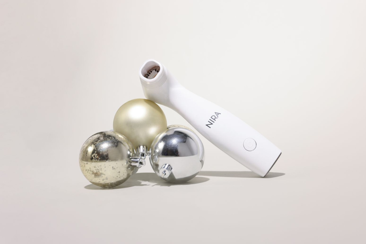 NIRA Precision Laser surrounded by holiday ornaments, highlighting portable at-home laser skincare for wrinkle reduction and skin rejuvenation.