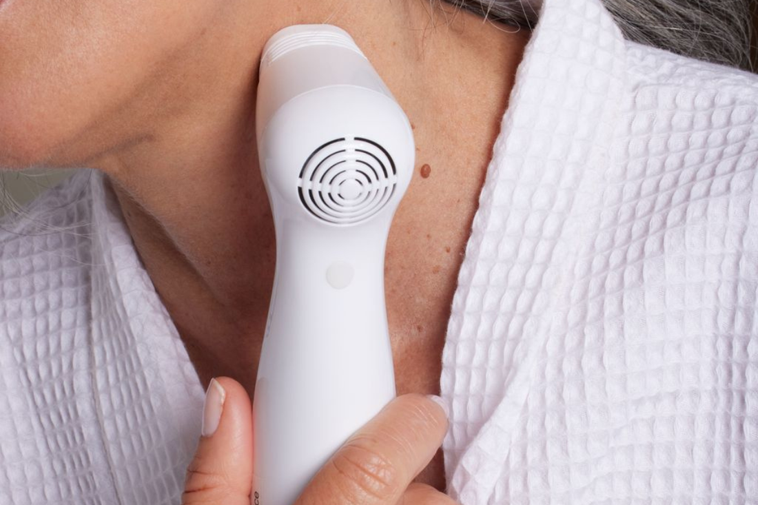 Older woman using NIRA at-home laser on her neck to improve skin firmness and reduce signs of aging.