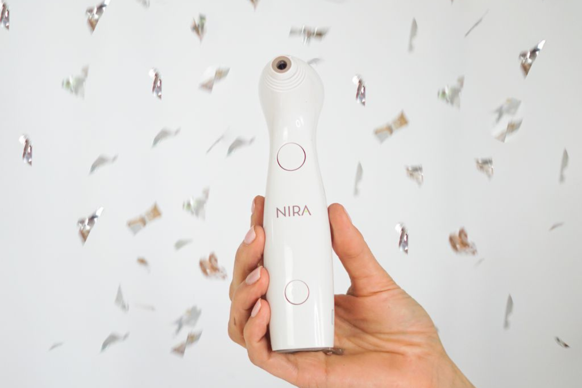 Nira at-home laser device held in front of the camera with silver confetti, showcasing a festive skincare glow.