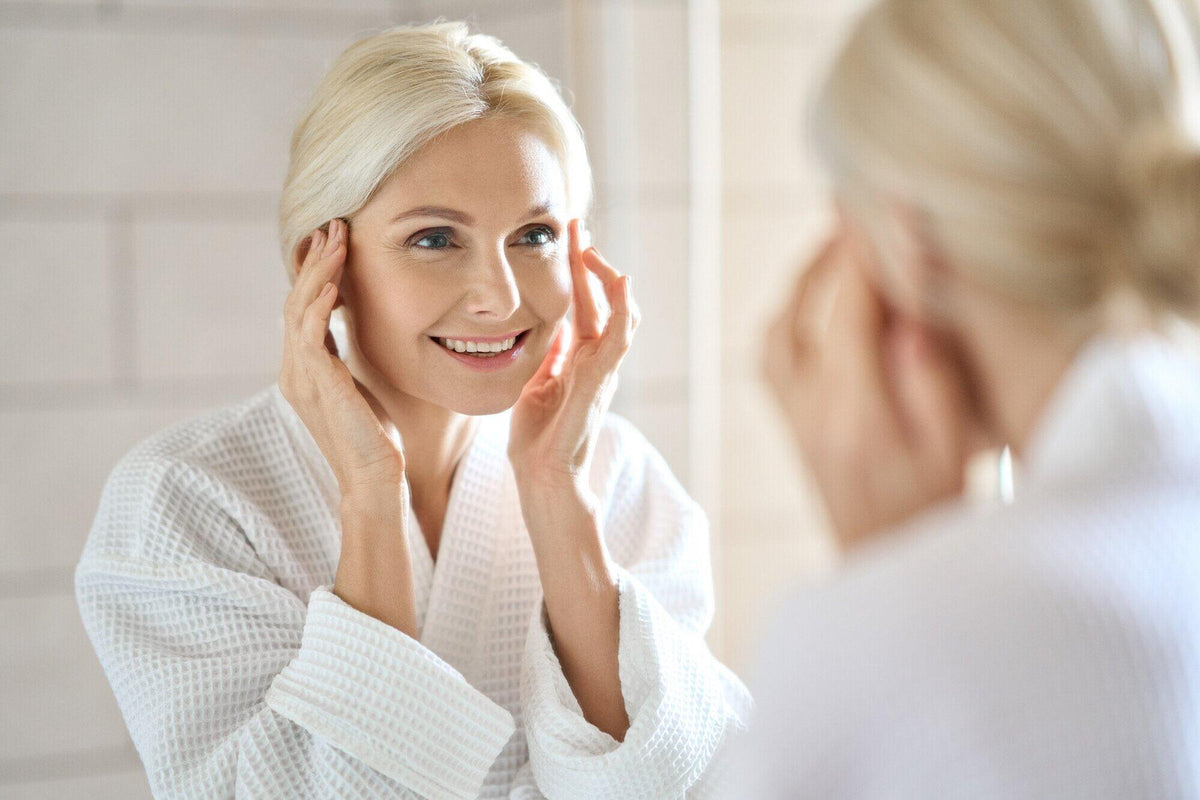 Woman touching her face in a bathroom mirror during her morning skincare routine